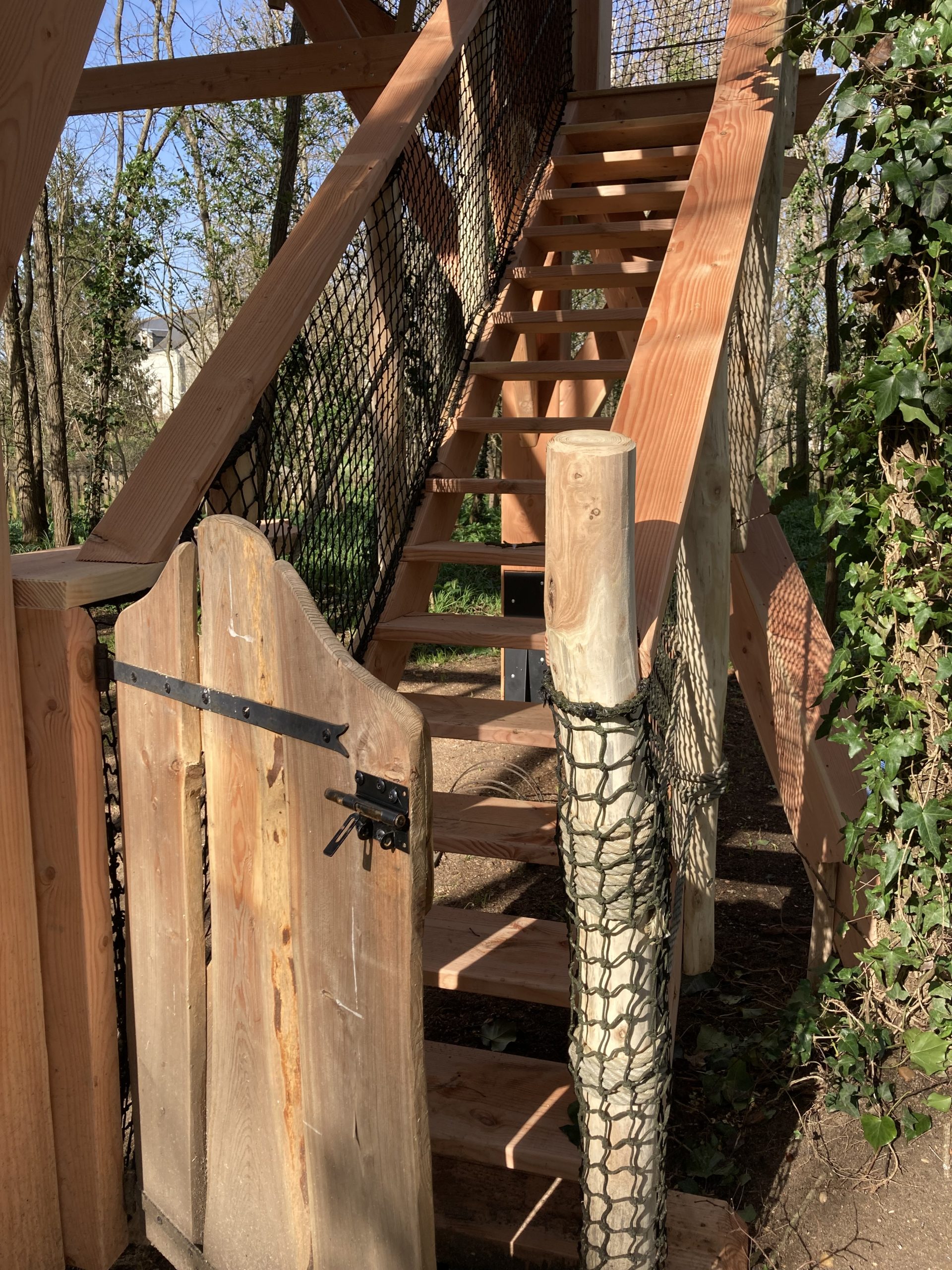 cabane perchée du pecheur_portail Escalier en bois menant à une cabane dans les arbres, entourée de verdure.