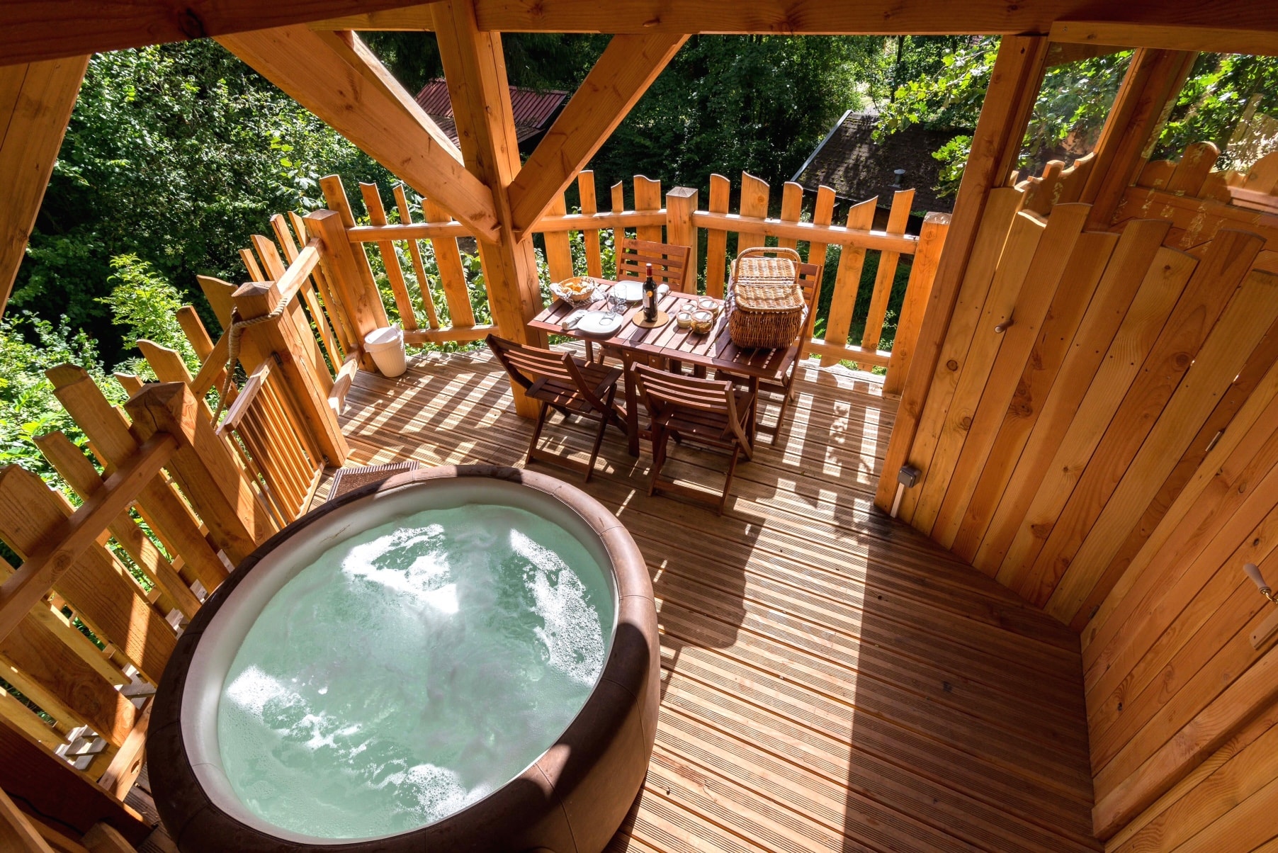 cabane spa Chene jacuzzi vue dessus Cabane perchée avec jacuzzi, entourée de verdure et dune terrasse en bois.