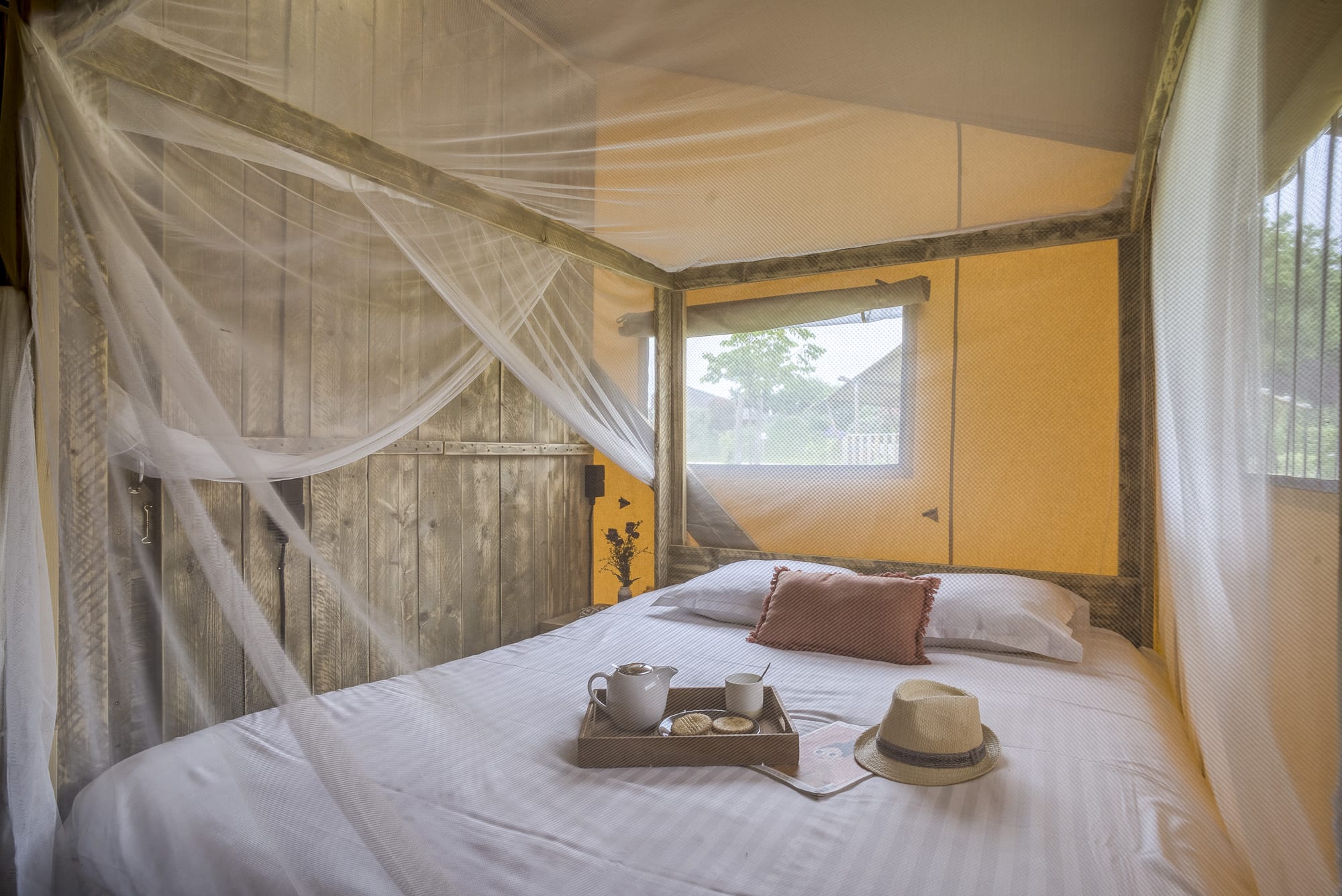 VFP_Topi_3 Chambre en cabane avec moustiquaire, décor chaleureux et vue sur la nature.