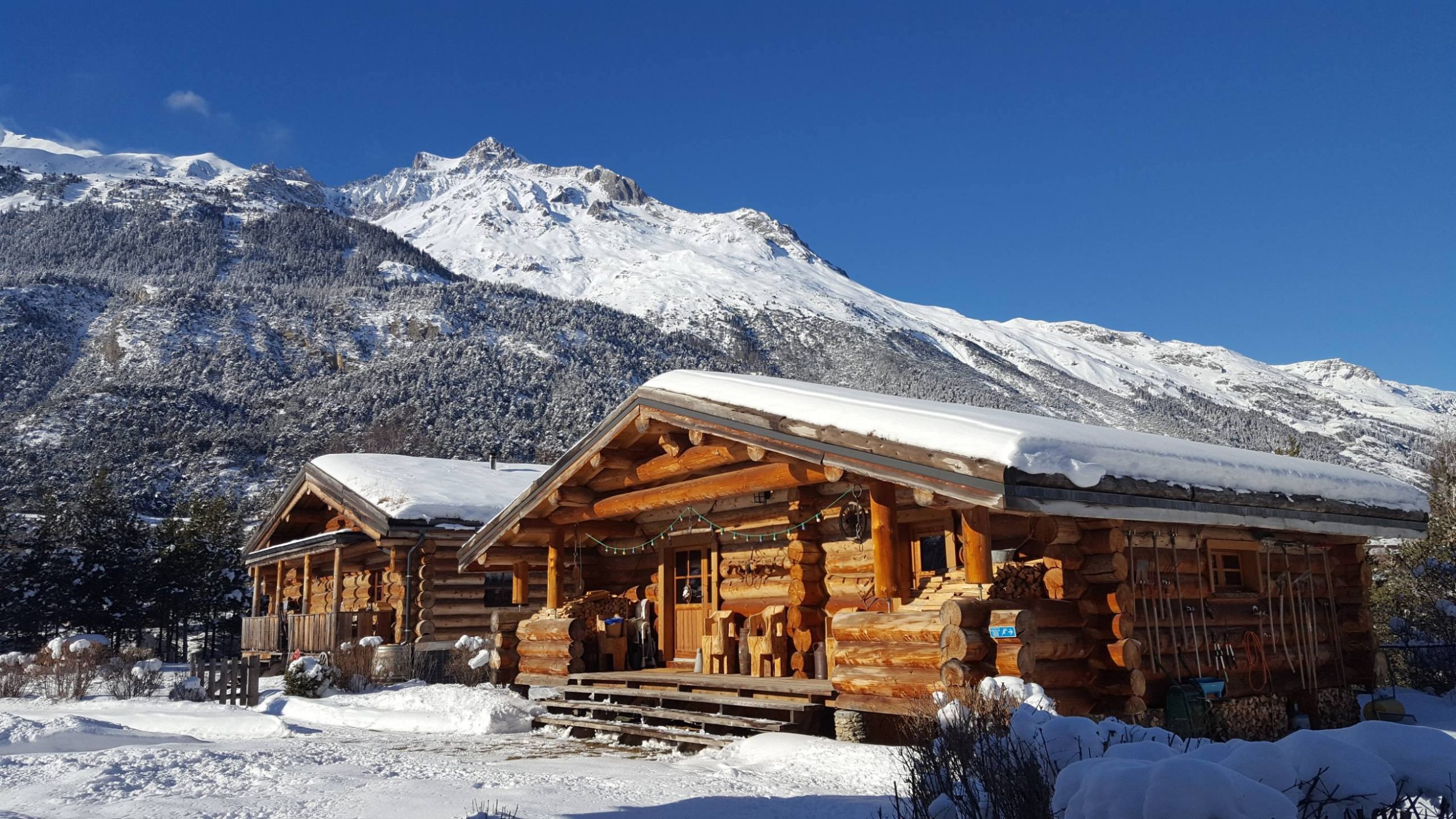 2 Parachée hiver Chalet en bois, entouré de neige, avec montagnes majestueuses en arrière-plan.