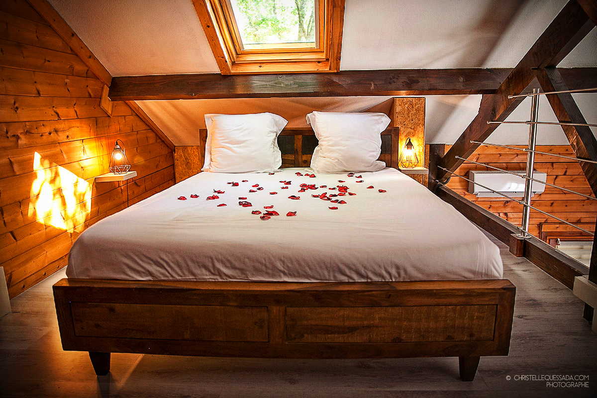 Domaine de La Male chalet spa insolite Chalet en bois avec lit décoré de pétales de roses, ambiance romantique et chaleureuse.
