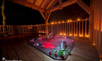 Cabane en bois avec jacuzzi romantique, éclairage doux et roses sur la terrasse.