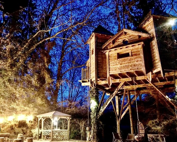 cabane ile la nuit Cabane perchée en bois à la lueur des lanternes, entourée darbres.