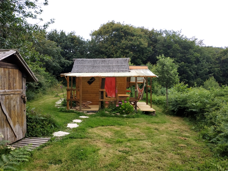 cahutte 8 Cabane en bois à Basse-Normandie, entourée de verdure et dun chemin de pierres.