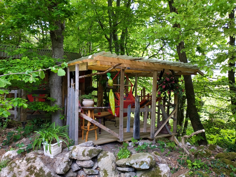 nid extérieur 2022 2 Cabane en bois nichée dans la verdure, avec un hamac coloré et des fleurs.