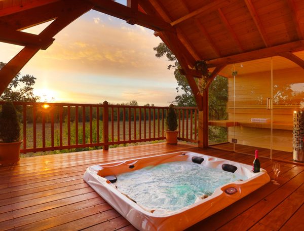 Cabane en bois avec jacuzzi extérieur, vue sur le coucher de soleil.