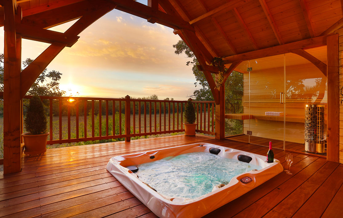 Cabane en bois avec jacuzzi extérieur, vue sur le coucher de soleil.