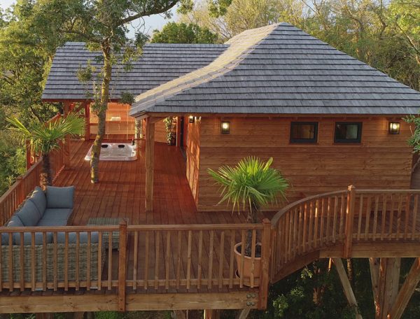 Cabane perchée en bois dans les arbres, avec terrasse et jacuzzi.