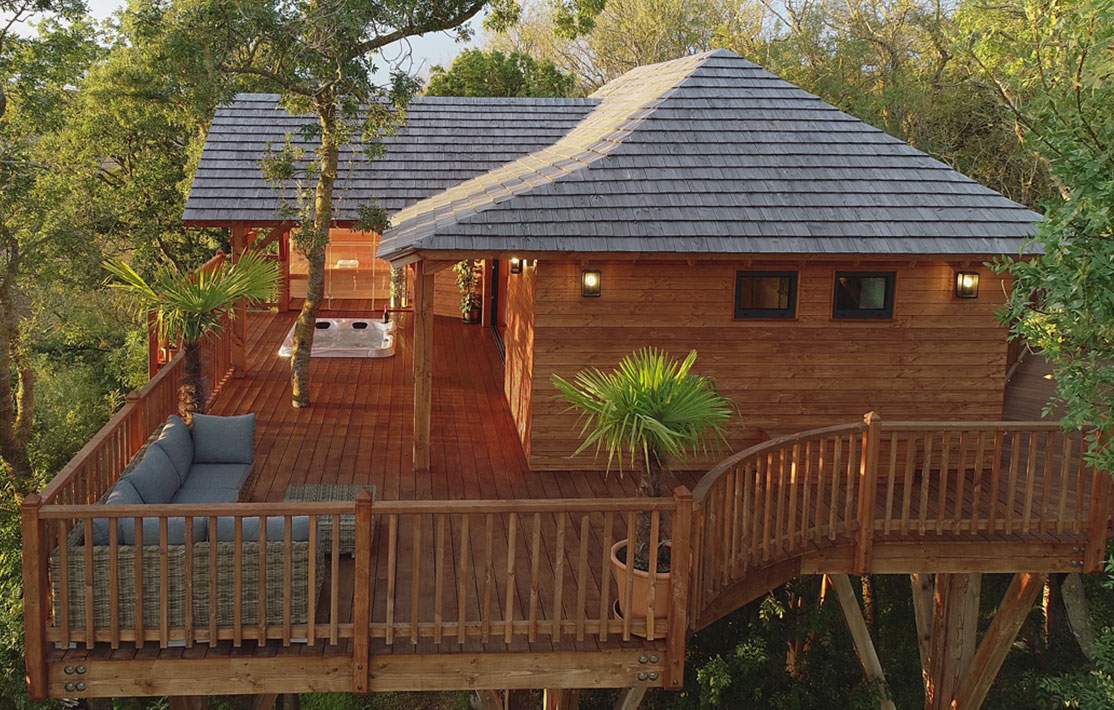 Cabane perchée en bois dans les arbres, avec terrasse et jacuzzi.