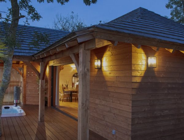 Cabane en bois avec jacuzzi, entourée de verdure au crépuscule.