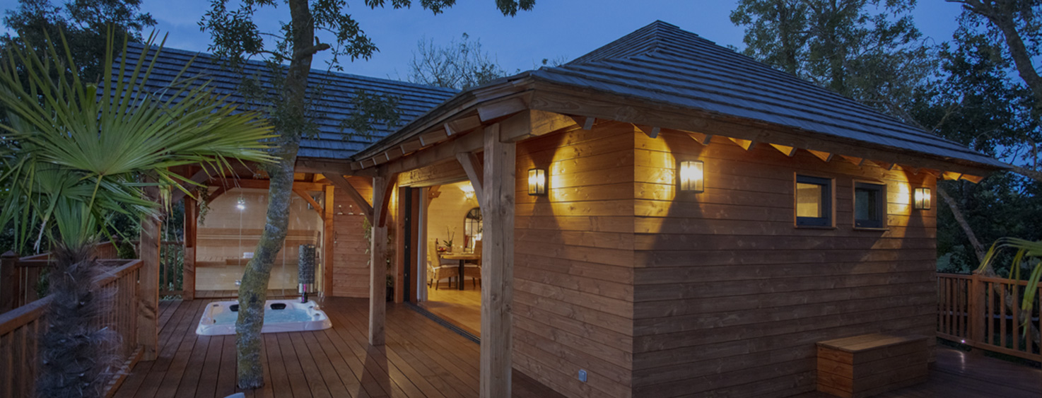 Cabane en bois avec jacuzzi, entourée de verdure au crépuscule.