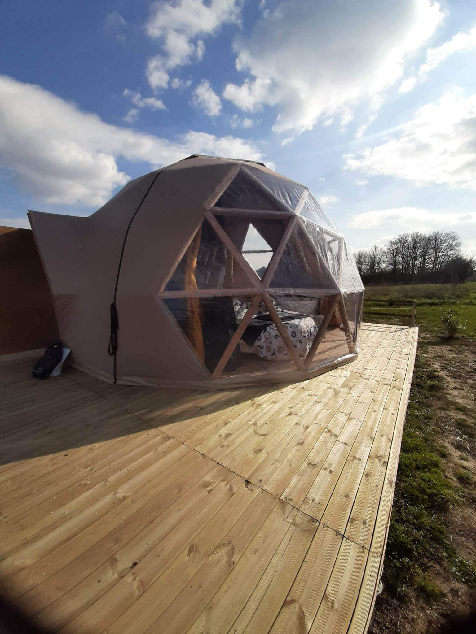 9D3C1413-2DEA-4D6B-9056-0DDA6A36A178 Dôme géodésique sur terrasse en bois, offrant une vue dégagée sur la nature.