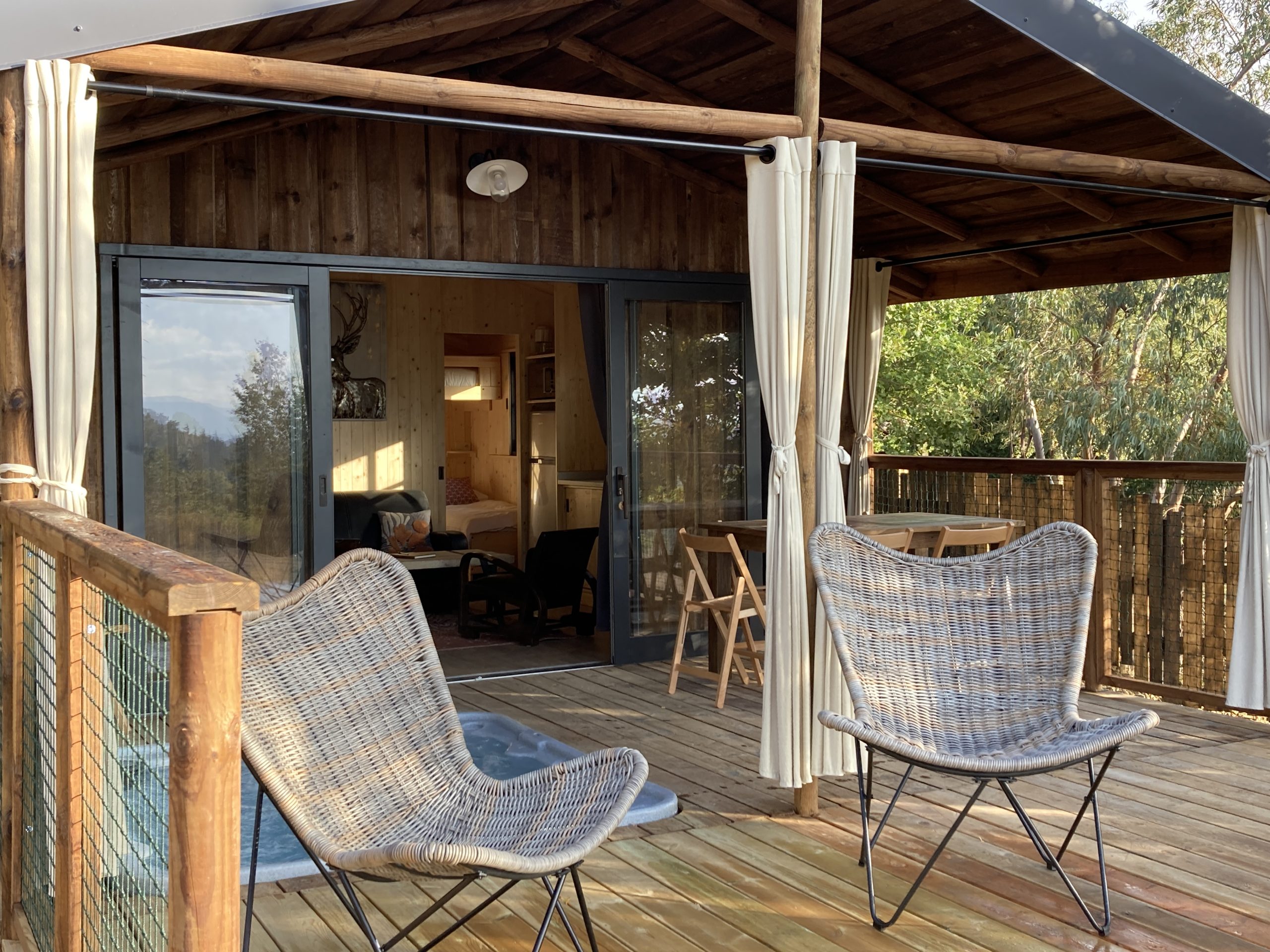IMG_1352 Cabane perchée en bois avec terrasse, chaises confortables et vue sur la nature.