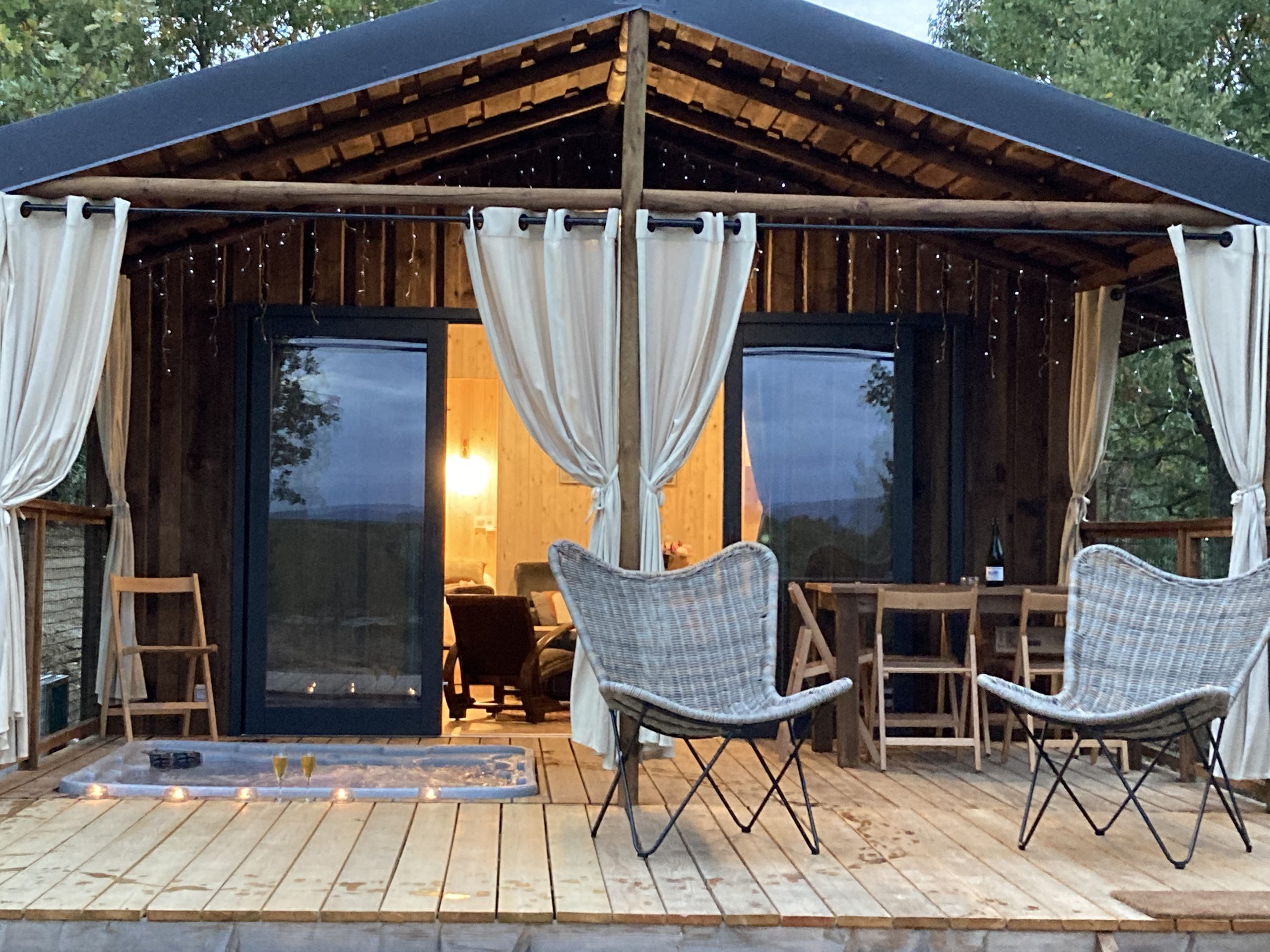 IMG_1432 Cabane en bois avec terrasse, éclairage doux et chaises confortables.