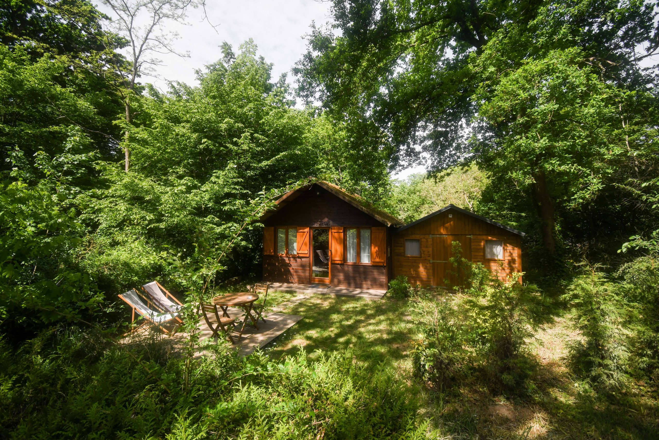 Passage secret cabane Bois de Rosoy crédit - Jordan Sapally Mai 2022 (3) Cabane en bois nichée dans la verdure, avec chaises longues et terrasse accueillante.