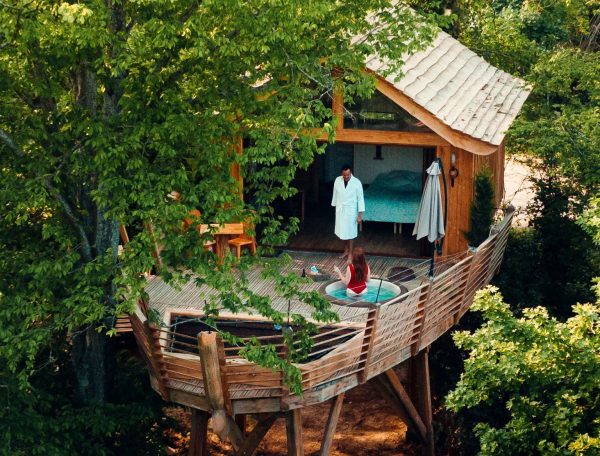 Cabane perchée dans les arbres, avec terrasse et vue sur la nature environnante.