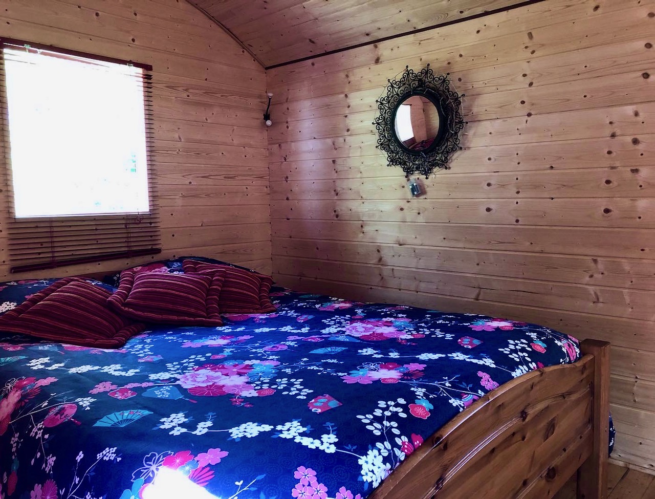 ROULOTTE NATURE ET CHARME - 1 (10) Chalet en bois à Basse-Normandie, intérieur chaleureux avec lit douillet et décor floral.