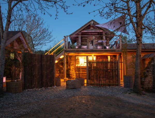 Cabane en bois illuminée, entourée darbres, offrant un cadre unique en Midi-Pyrénées.