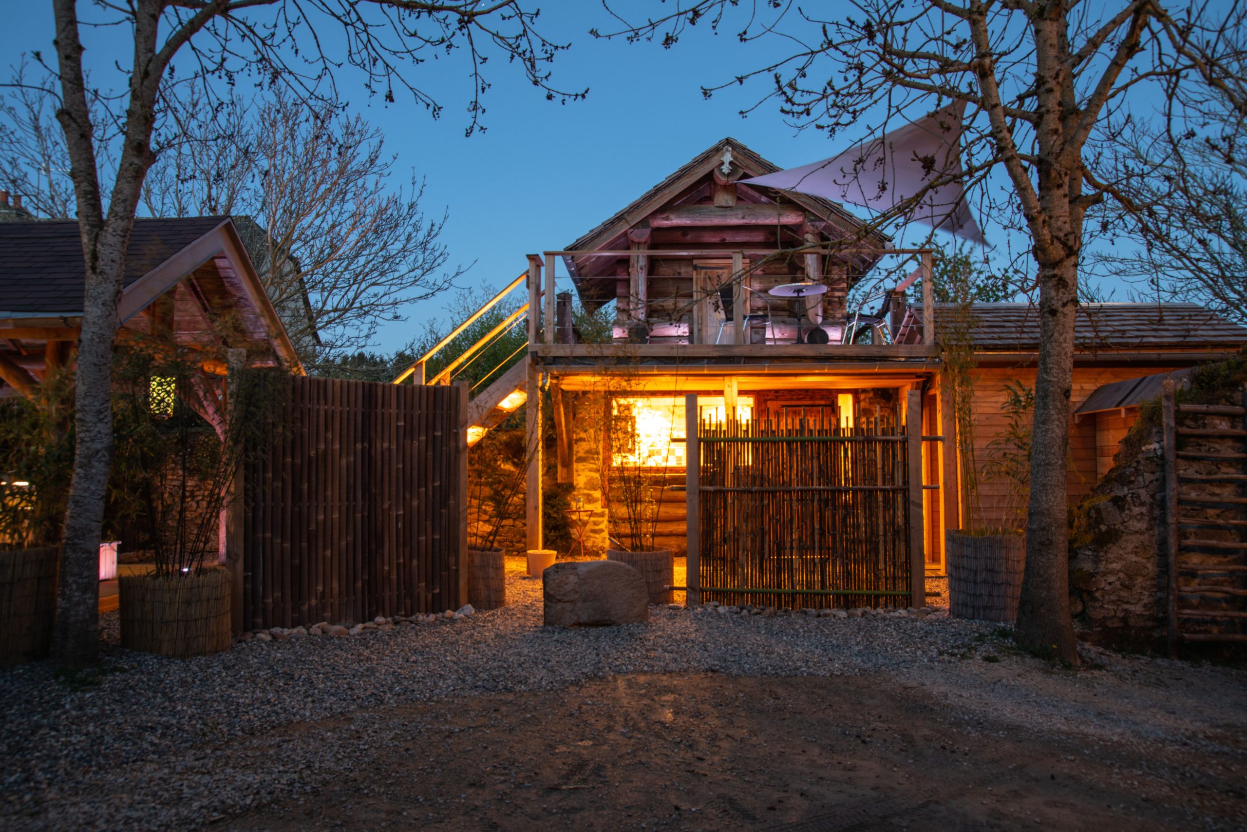 Cabane en bois illuminée, entourée darbres, offrant un cadre unique en Midi-Pyrénées.