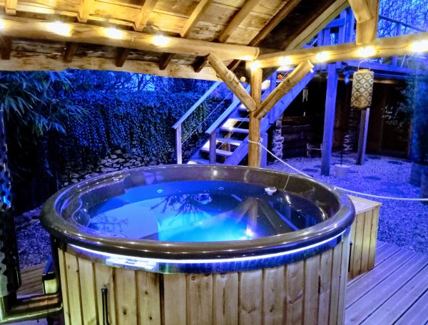 Hébergement insolite en Midi-Pyrénées avec jacuzzi illuminé sous une pergola en bois.