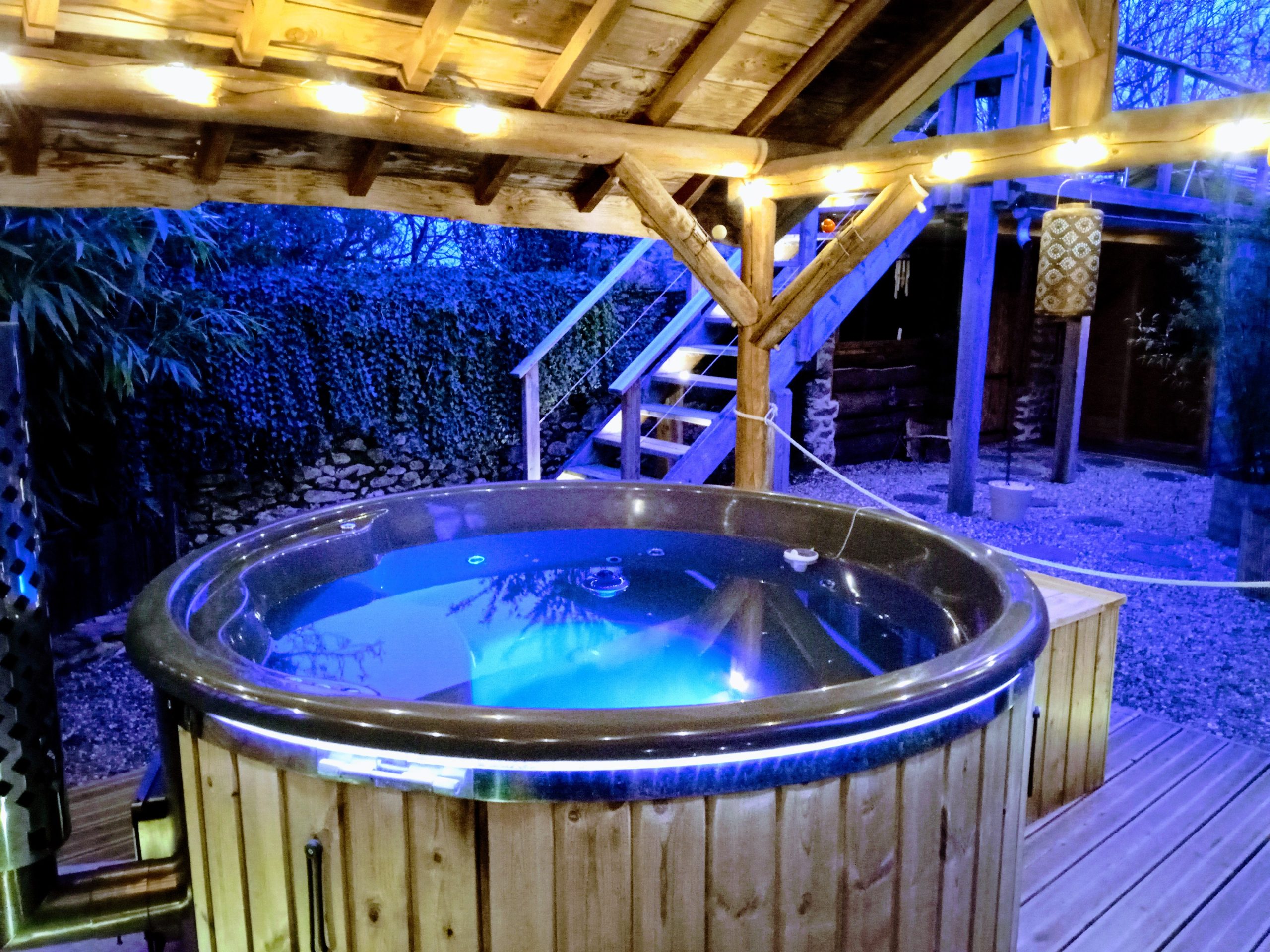 Hébergement insolite en Midi-Pyrénées avec jacuzzi illuminé sous une pergola en bois.