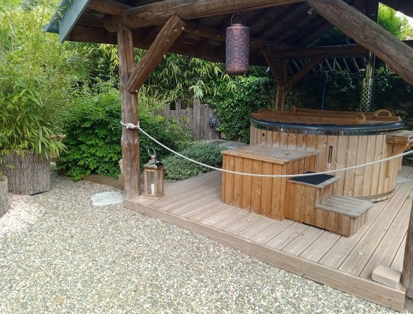 Hébergement insolite en Midi-Pyrénées avec un jacuzzi en bois entouré de verdure.
