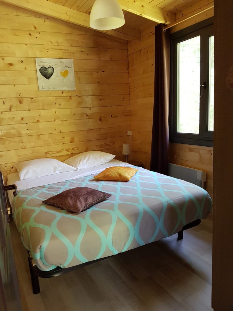 gretel8 Chalet en bois à Champagne-Ardennes, chambre cosy avec lit double et décor chaleureux.