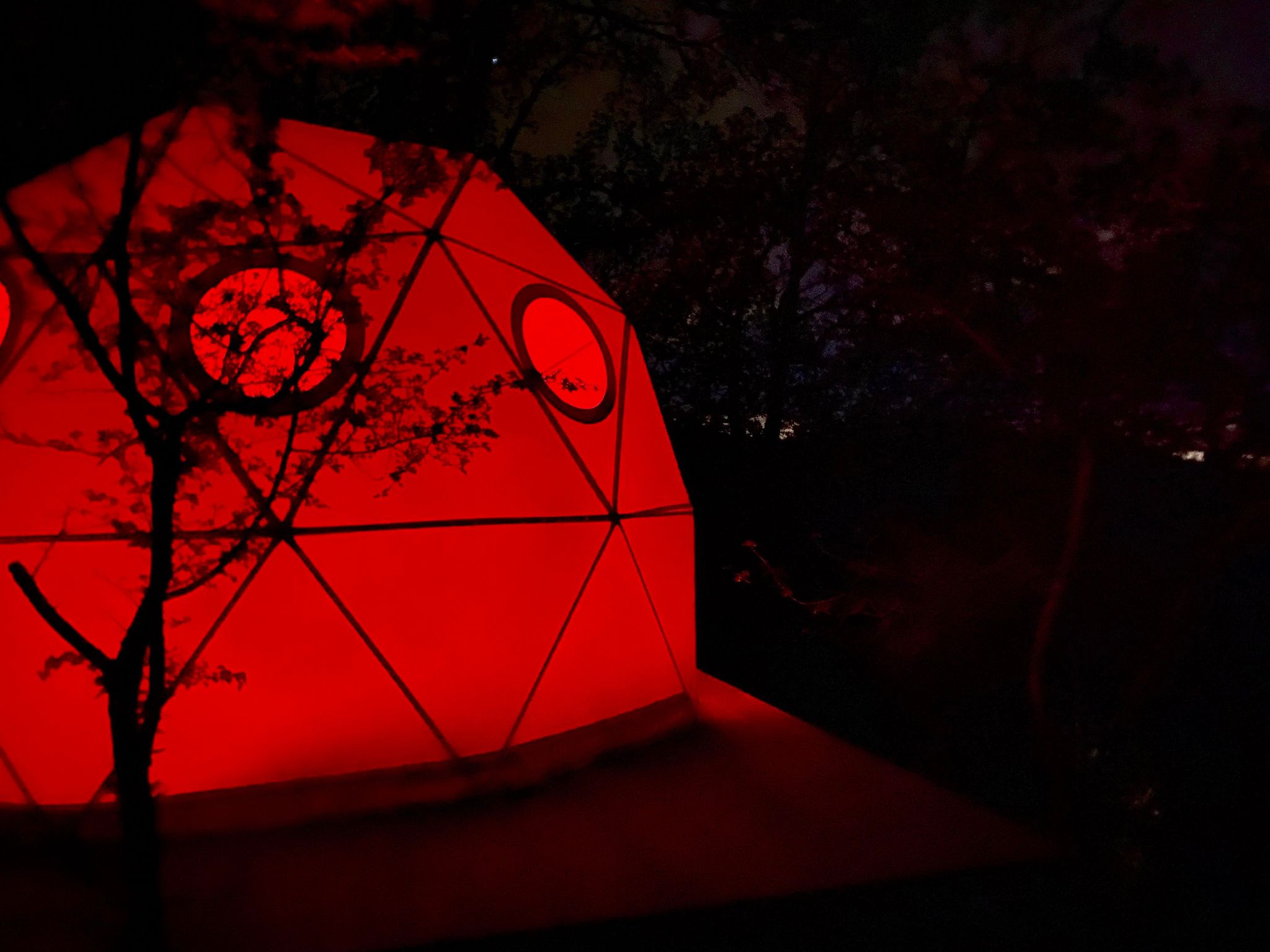 Dôme géodésique illuminé en rouge, niché dans la nature du Languedoc-Roussillon.