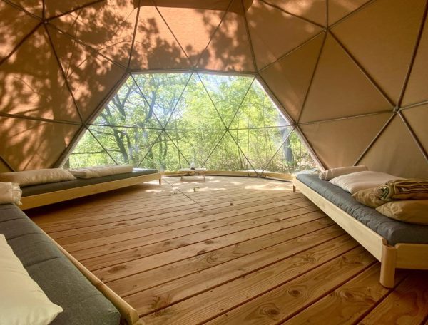 Dôme géodésique en bois, intérieur lumineux avec lits confortables et vue sur la nature.