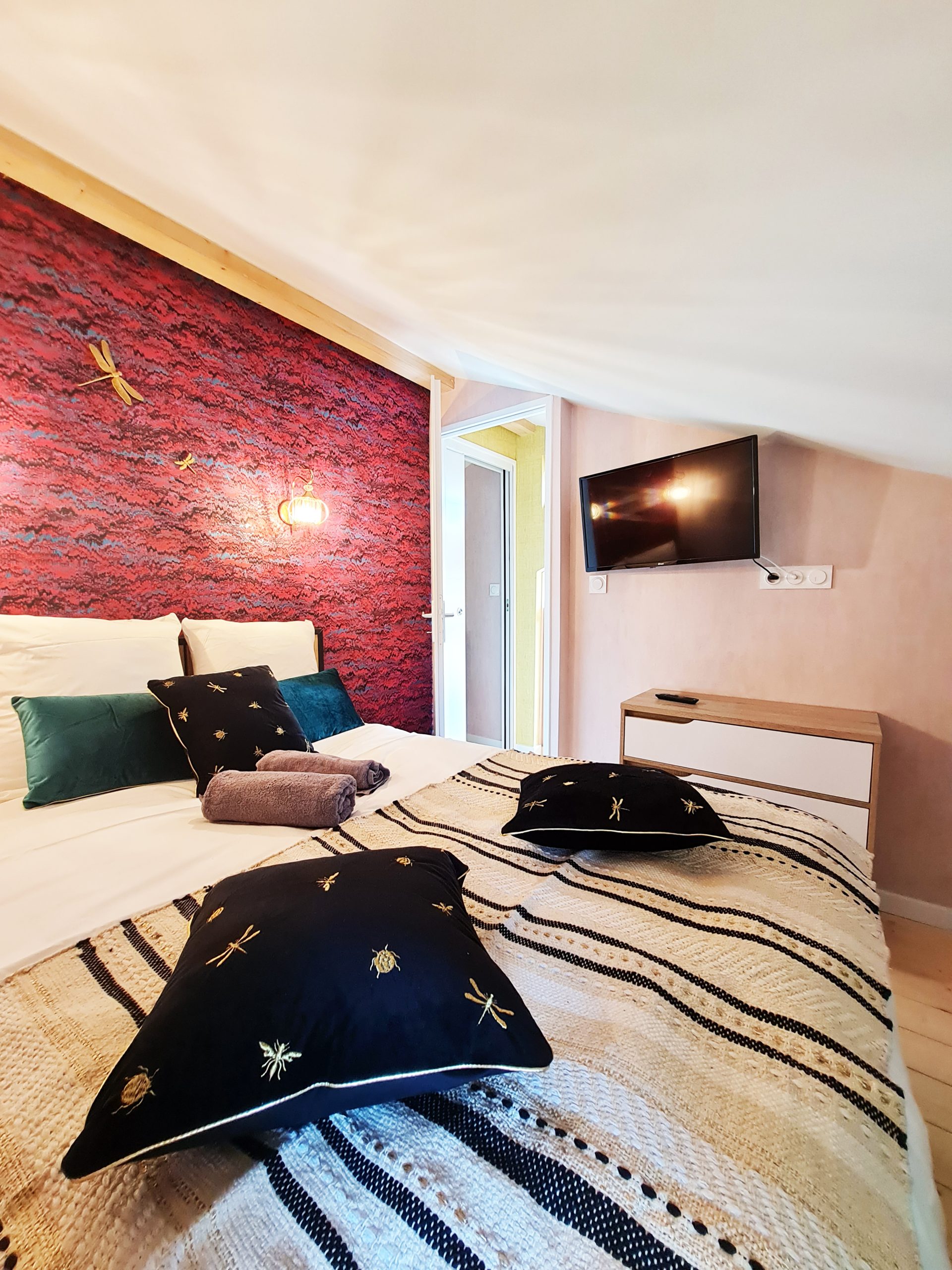 Cabane l'Enchantée - chambre Chambre cosy dans un hébergement insolite, avec mur en briques rouges et coussins décoratifs.