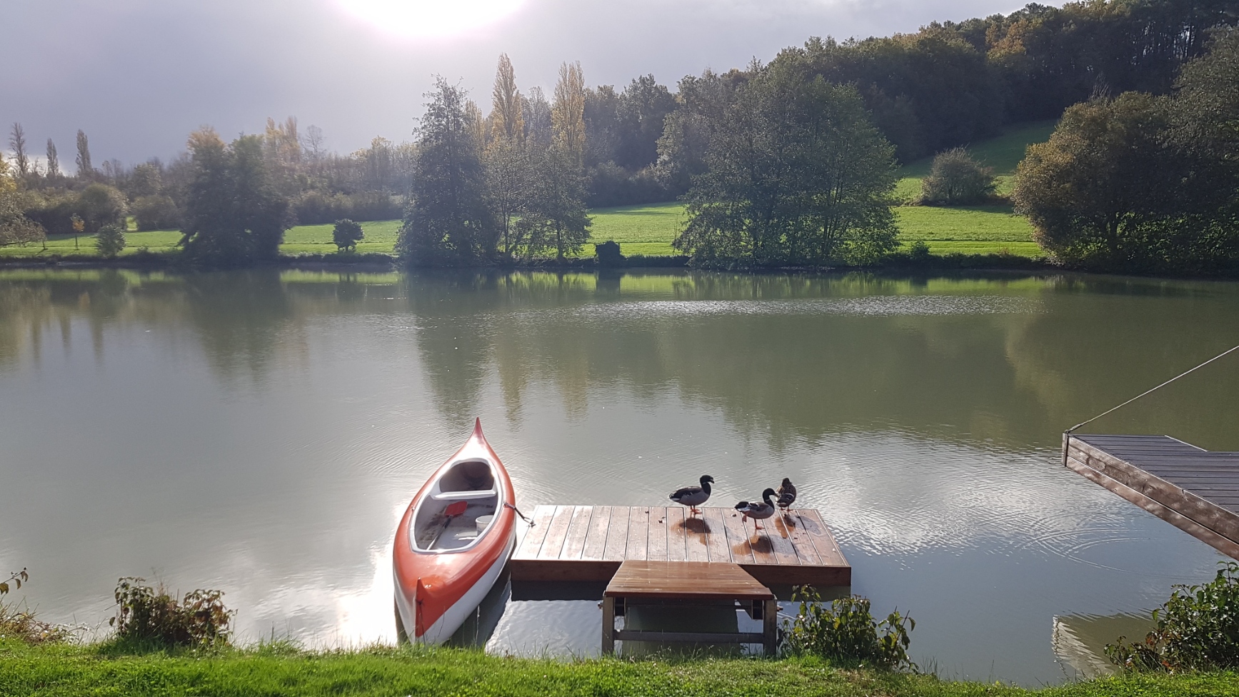 20201026_095400 Hébergement insolite en Aquitaine, avec un canoë orange sur un lac paisible.