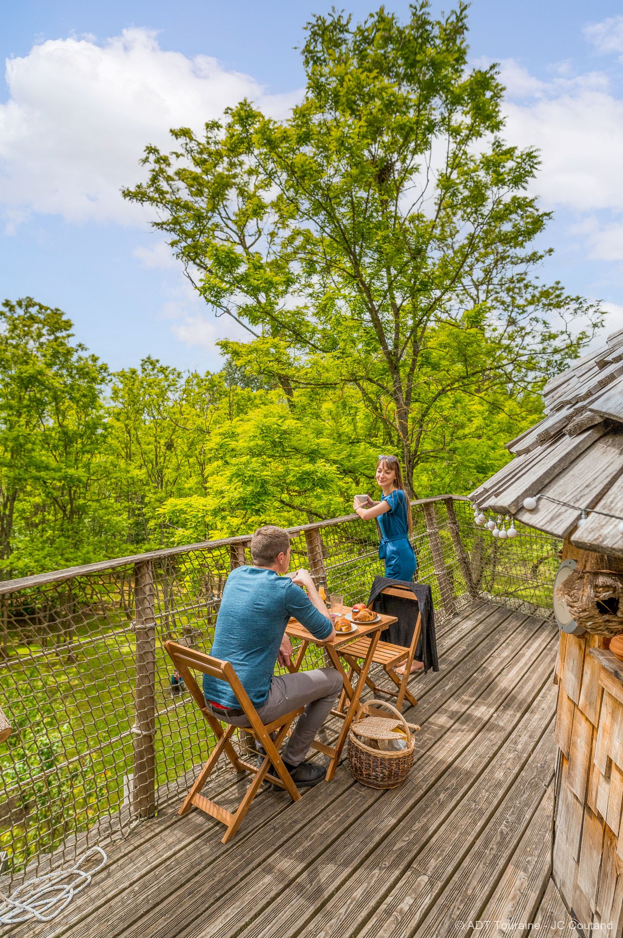 CabaneduVerger_Credit_ADT_terasse2 Cabane perchée dans les arbres, vue panoramique sur la nature verdoyante.