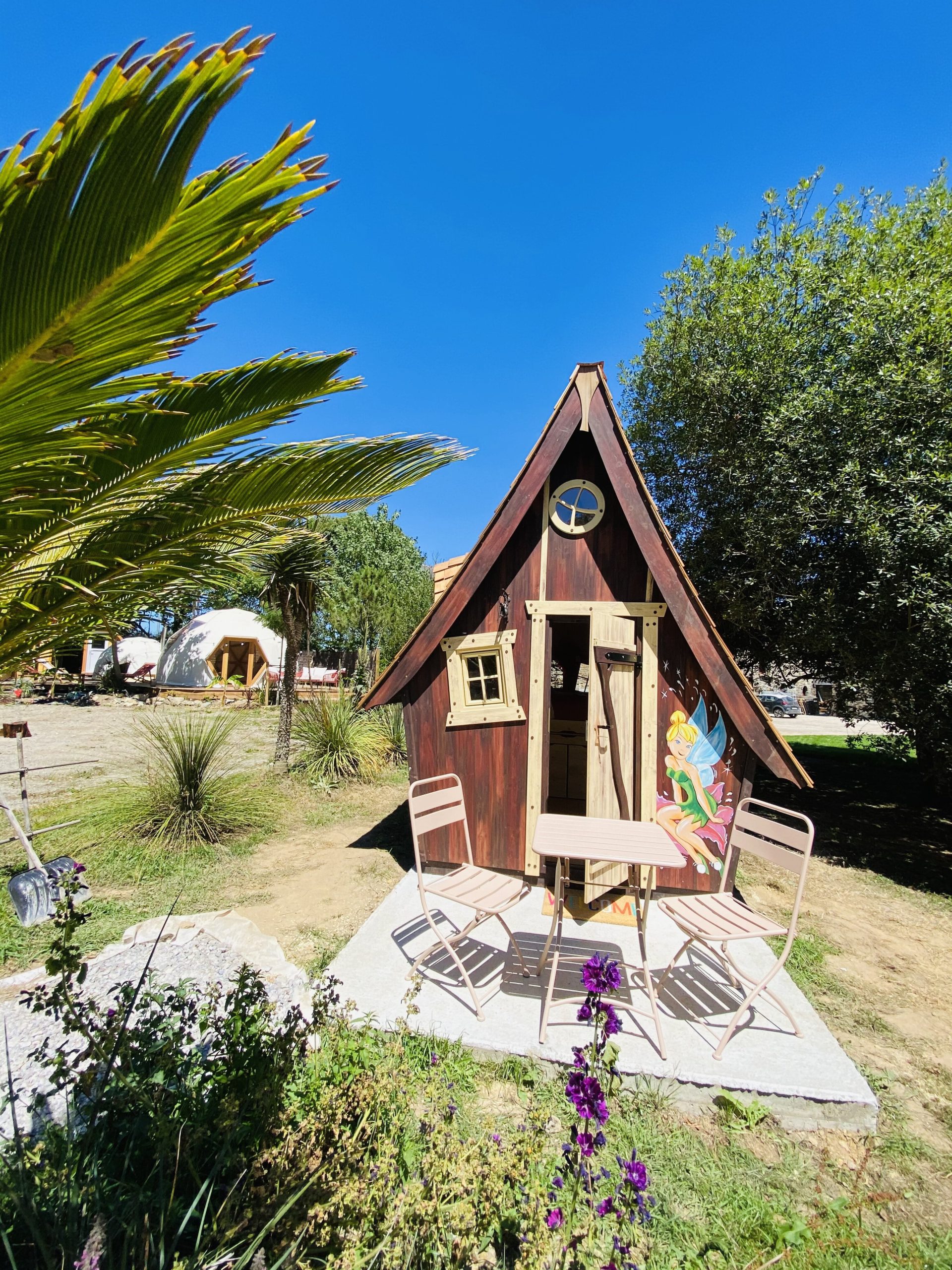 IMG_7782 Cabane en bois colorée en Bretagne, avec table et chaises sur la terrasse ensoleillée.