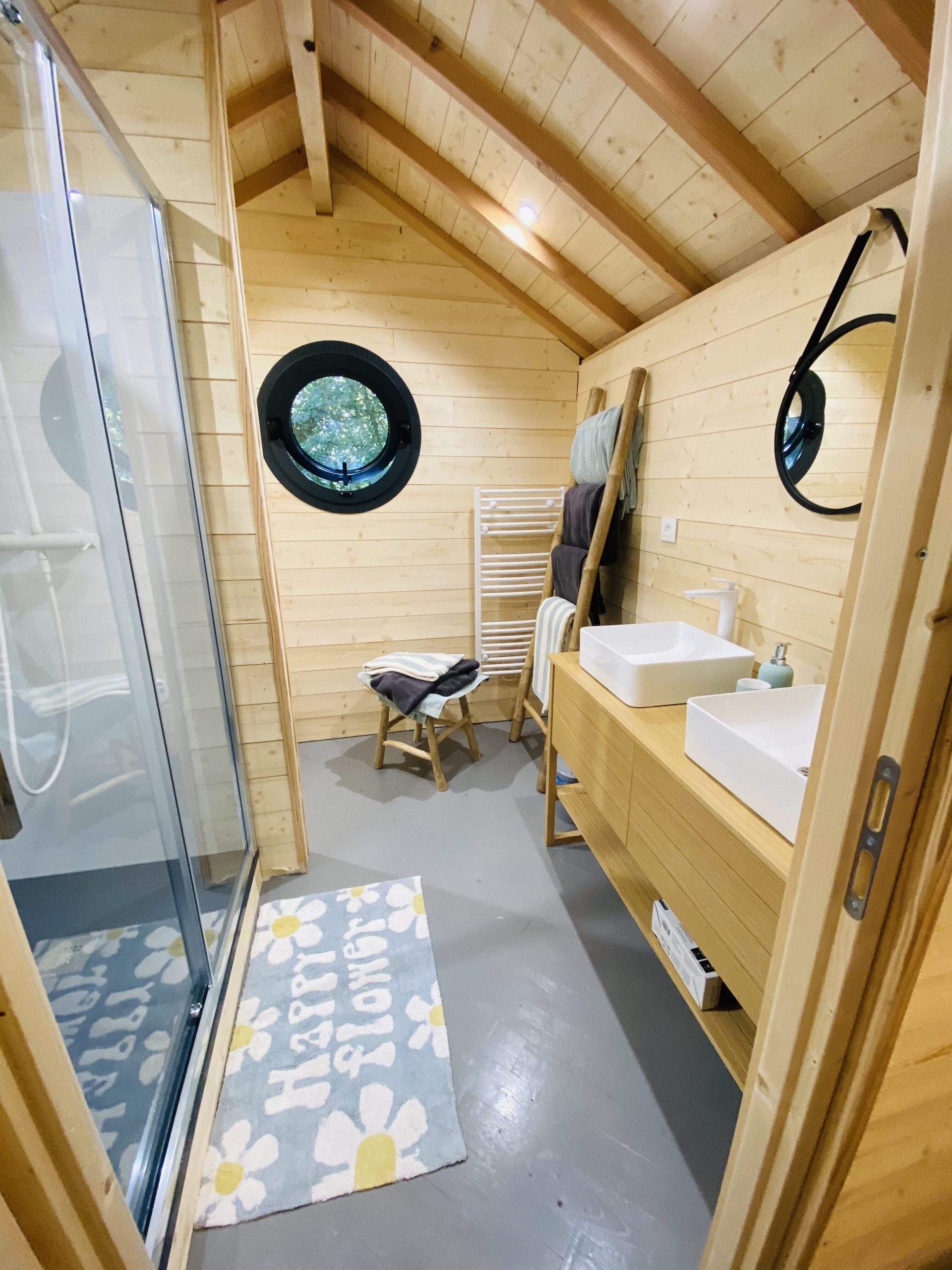 IMG_7829 Hébergement insolite en Bretagne : salle de bain en bois avec fenêtre ronde et douche spacieuse.