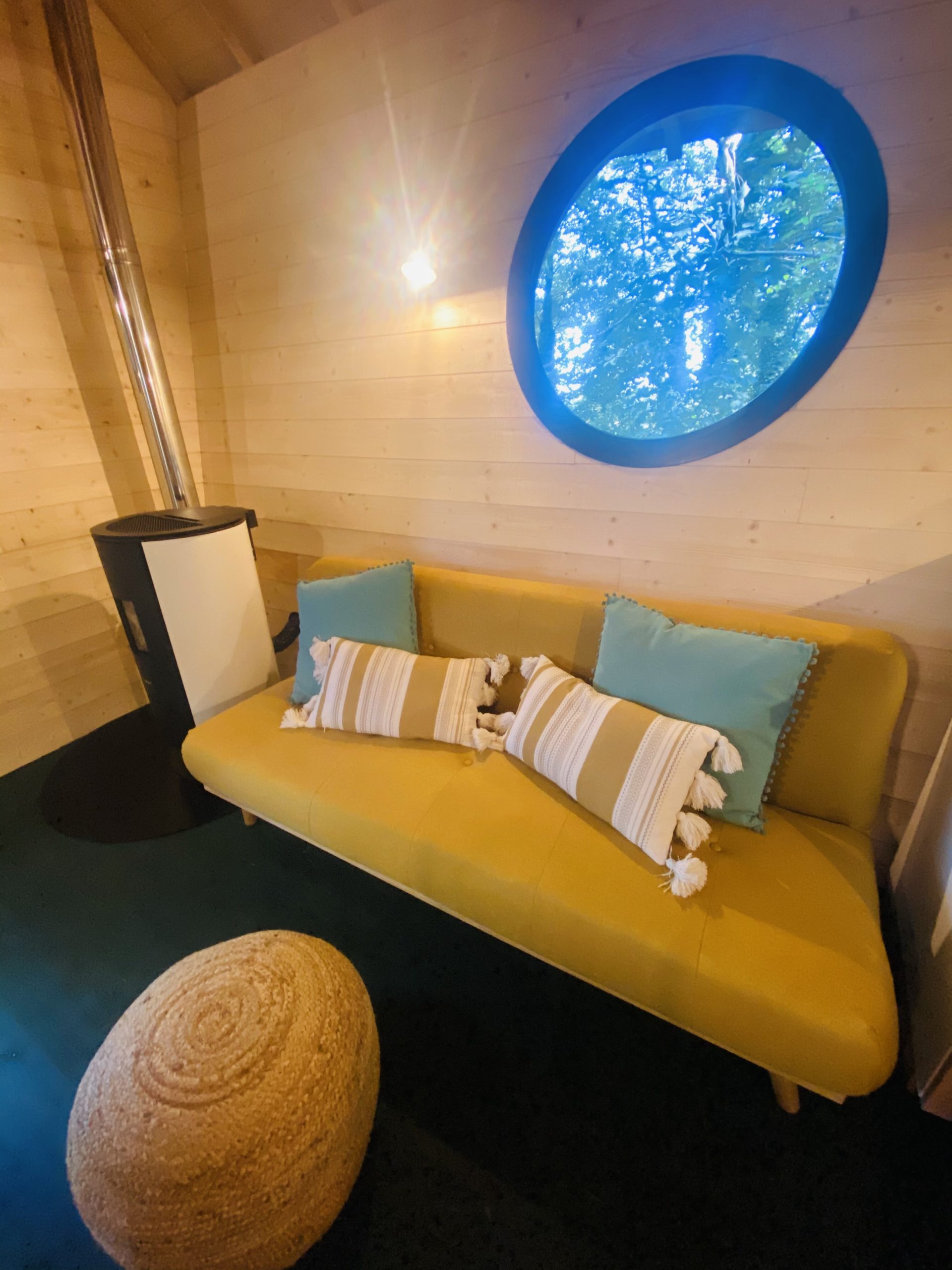IMG_7837 Hébergement insolite en Bretagne : intérieur cosy avec un canapé jaune et fenêtre ronde.