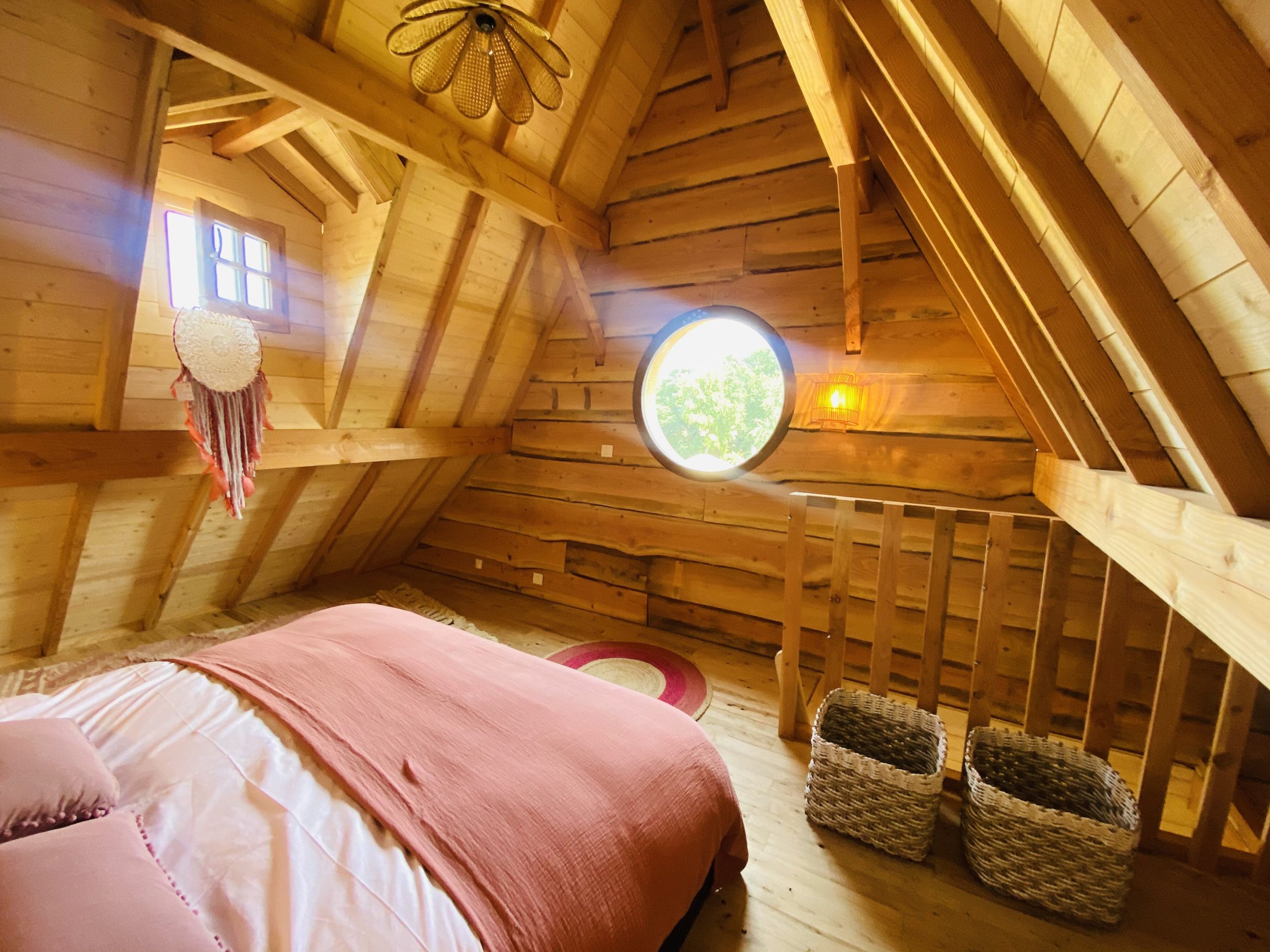 IMG_7902 Chalet en bois avec un lit douillet et une fenêtre ronde, ambiance chaleureuse.