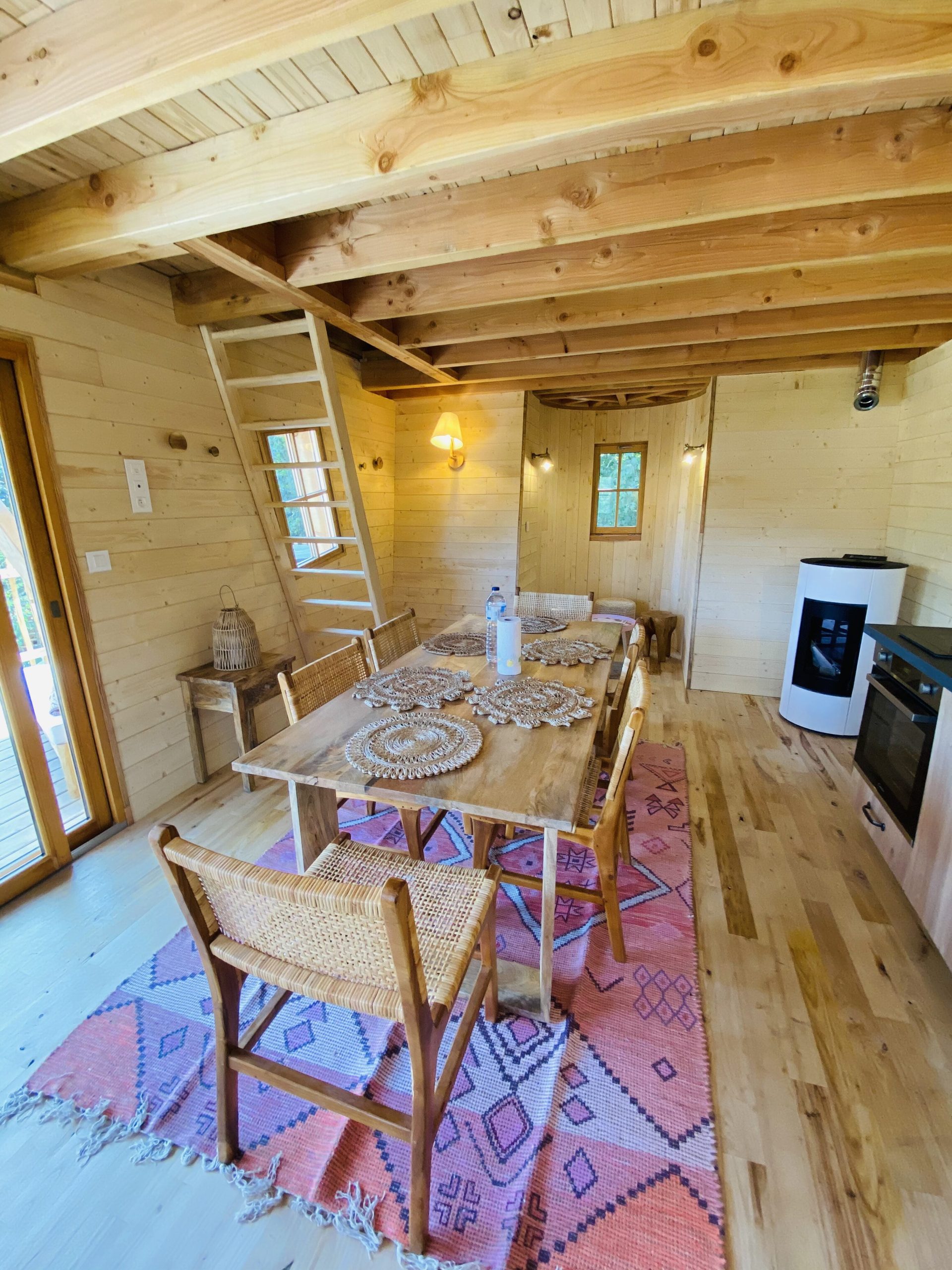IMG_7921 Cabane en bois en Bretagne, intérieur lumineux avec table en bois et tapis coloré.