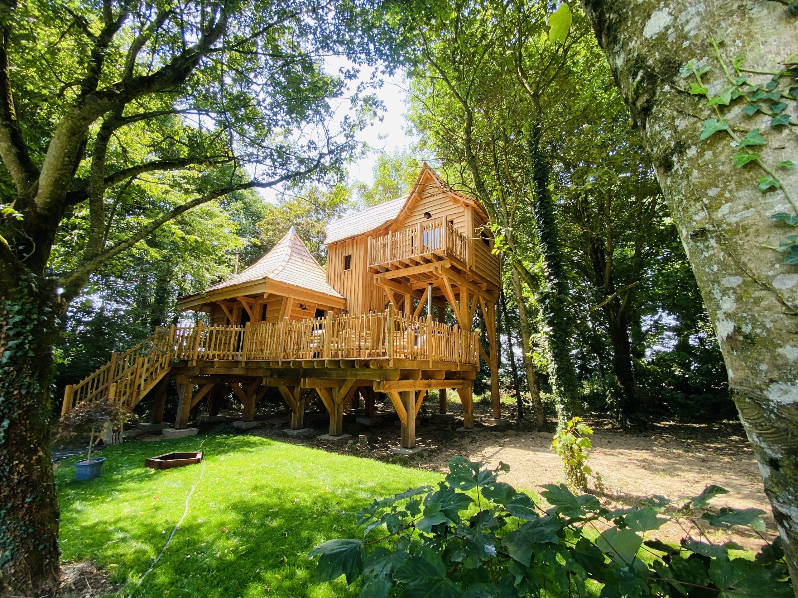 IMG_7960 Cabane en bois perchée dans les arbres, entourée de verdure en Bretagne.