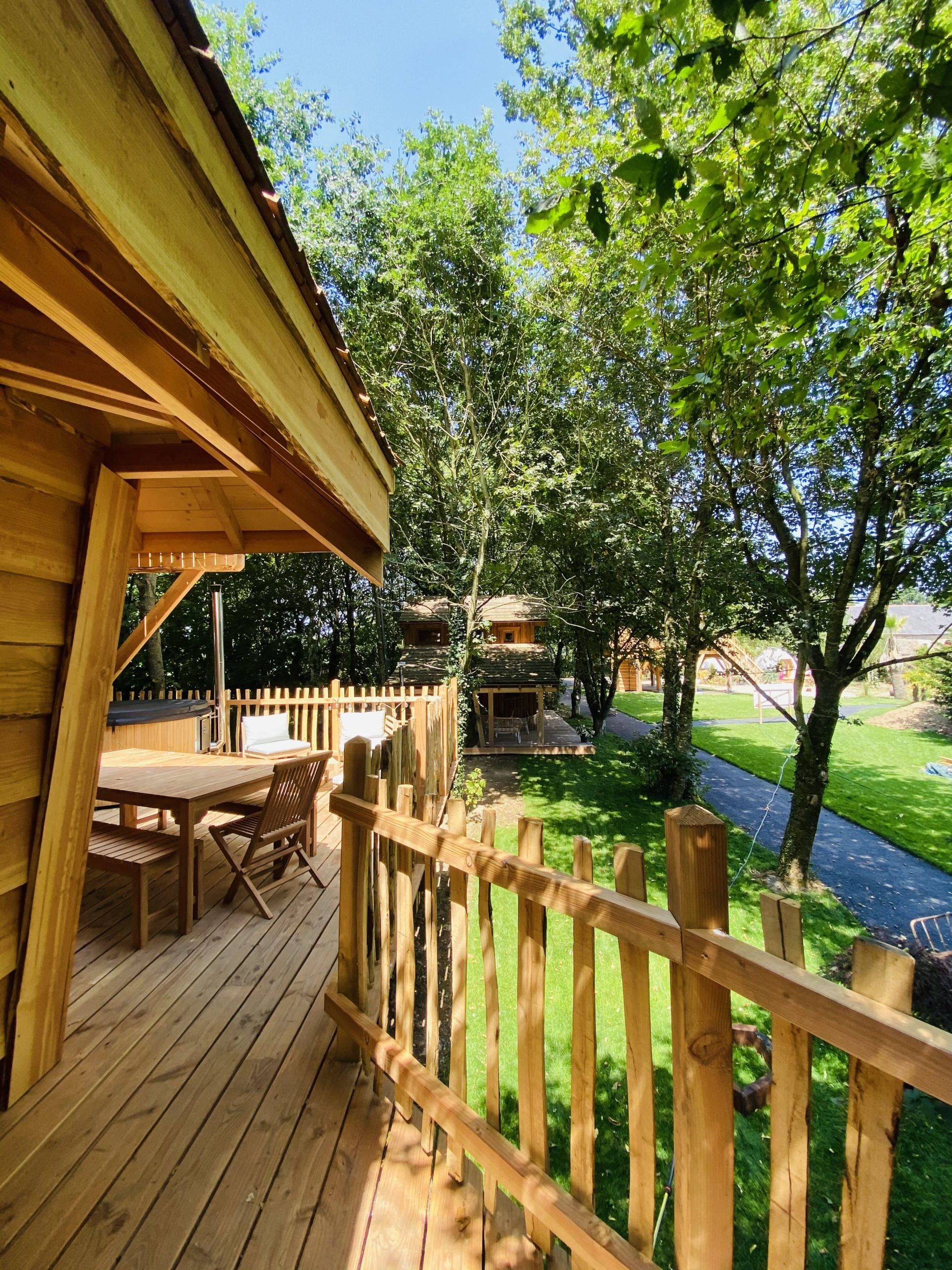 IMG_7961 Cabane en bois perchée, entourée darbres, avec terrasse ensoleillée.
