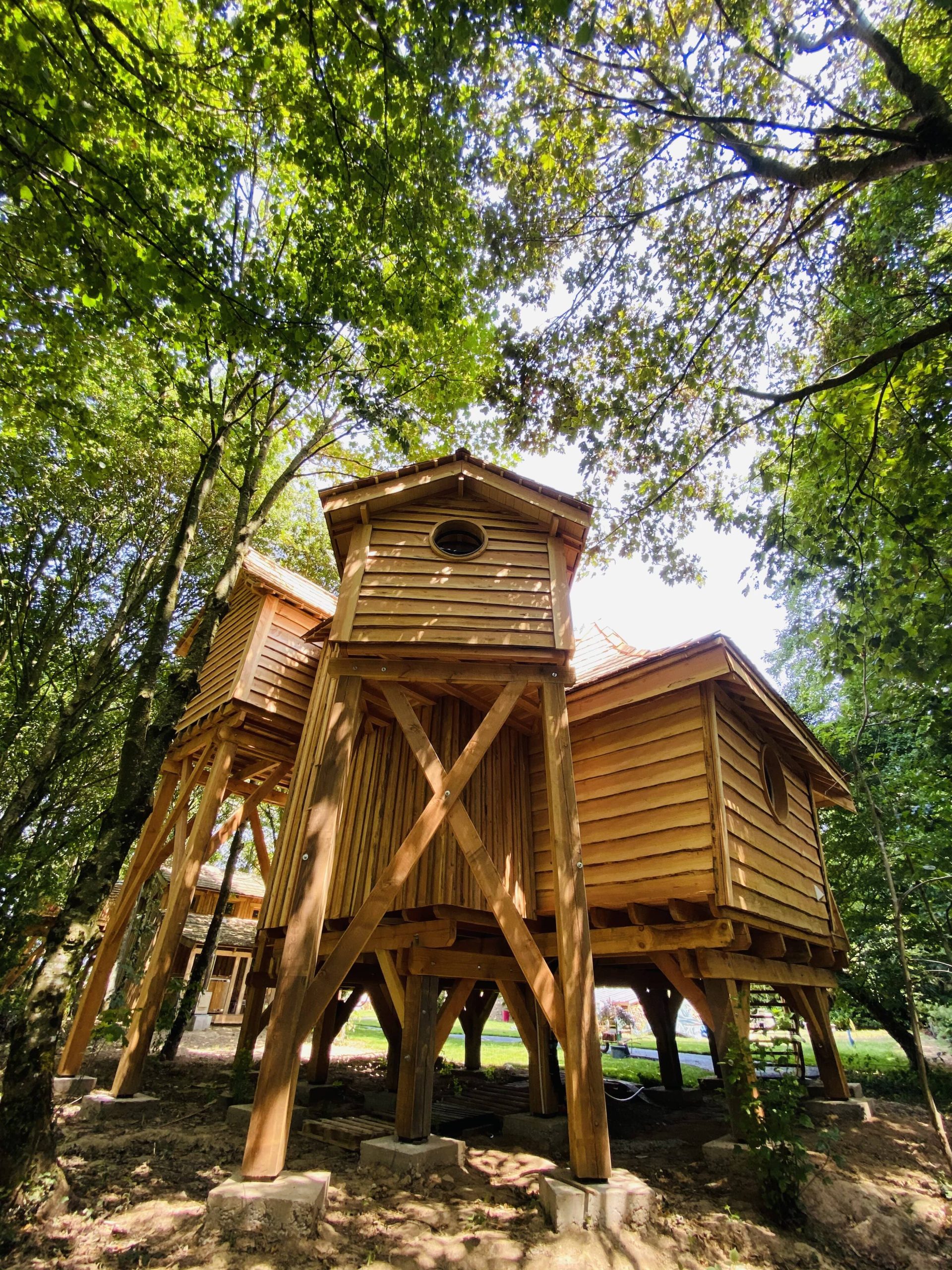 IMG_7964 Cabane perchée en bois, nichée dans les arbres en Bretagne, entourée de verdure.