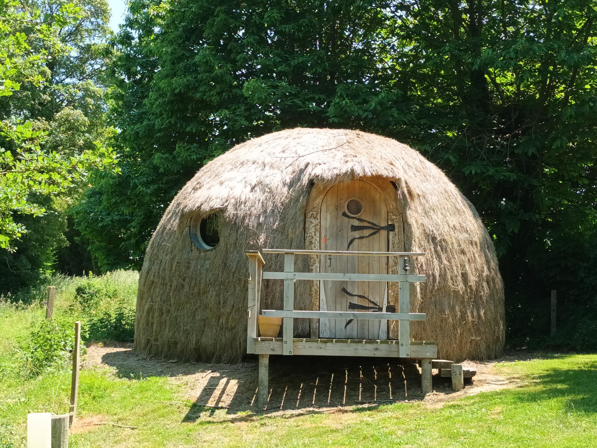 20230602_140613 Hébergement insolite en forme de dôme, recouvert de paille, dans un cadre verdoyant.