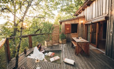 Cabane perchée en bois avec terrasse, ambiance cosy au milieu des arbres.