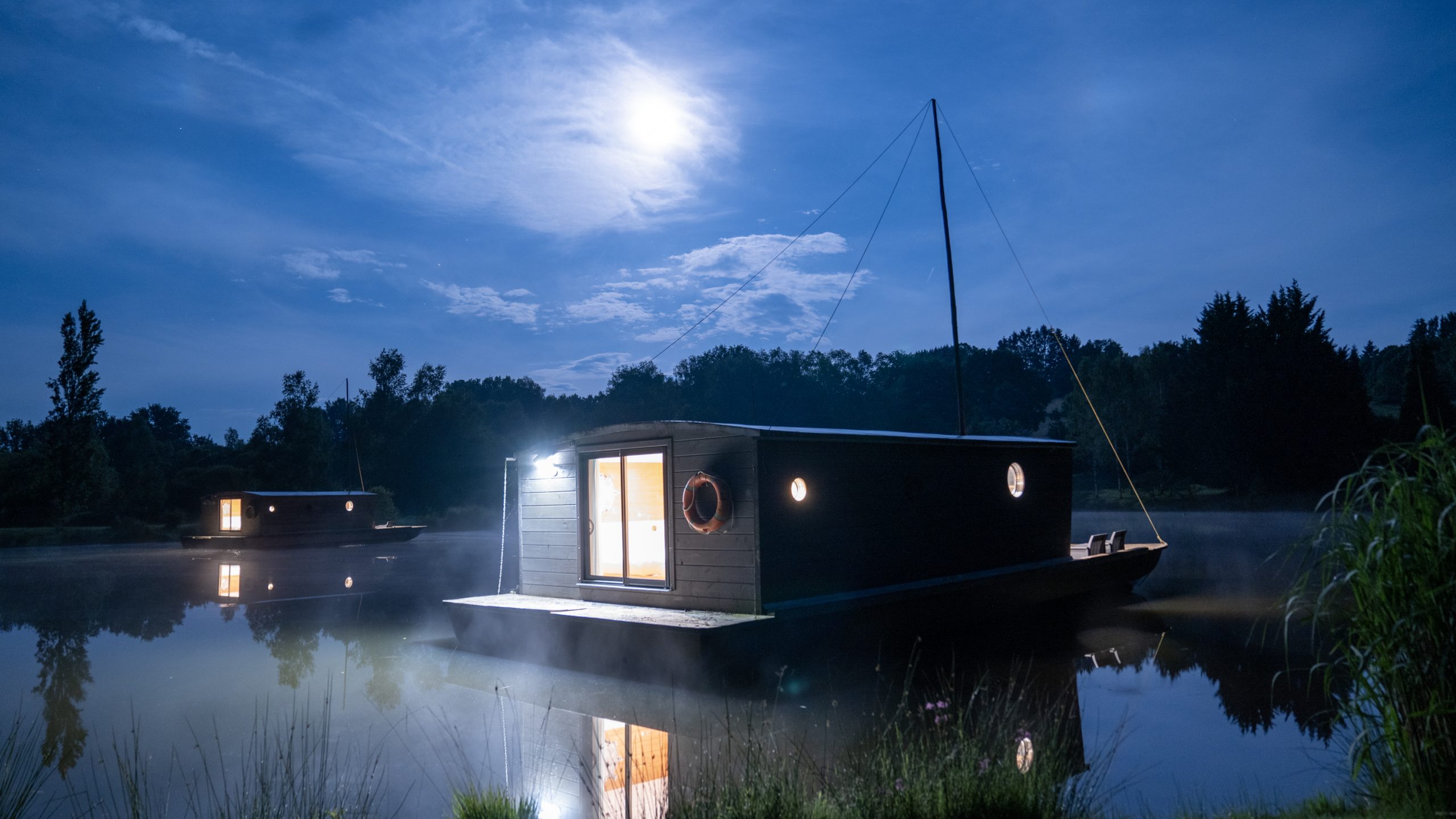 Chamberet_J1-157 Hébergement insolite : maison flottante illuminée sur un lac au clair de lune.