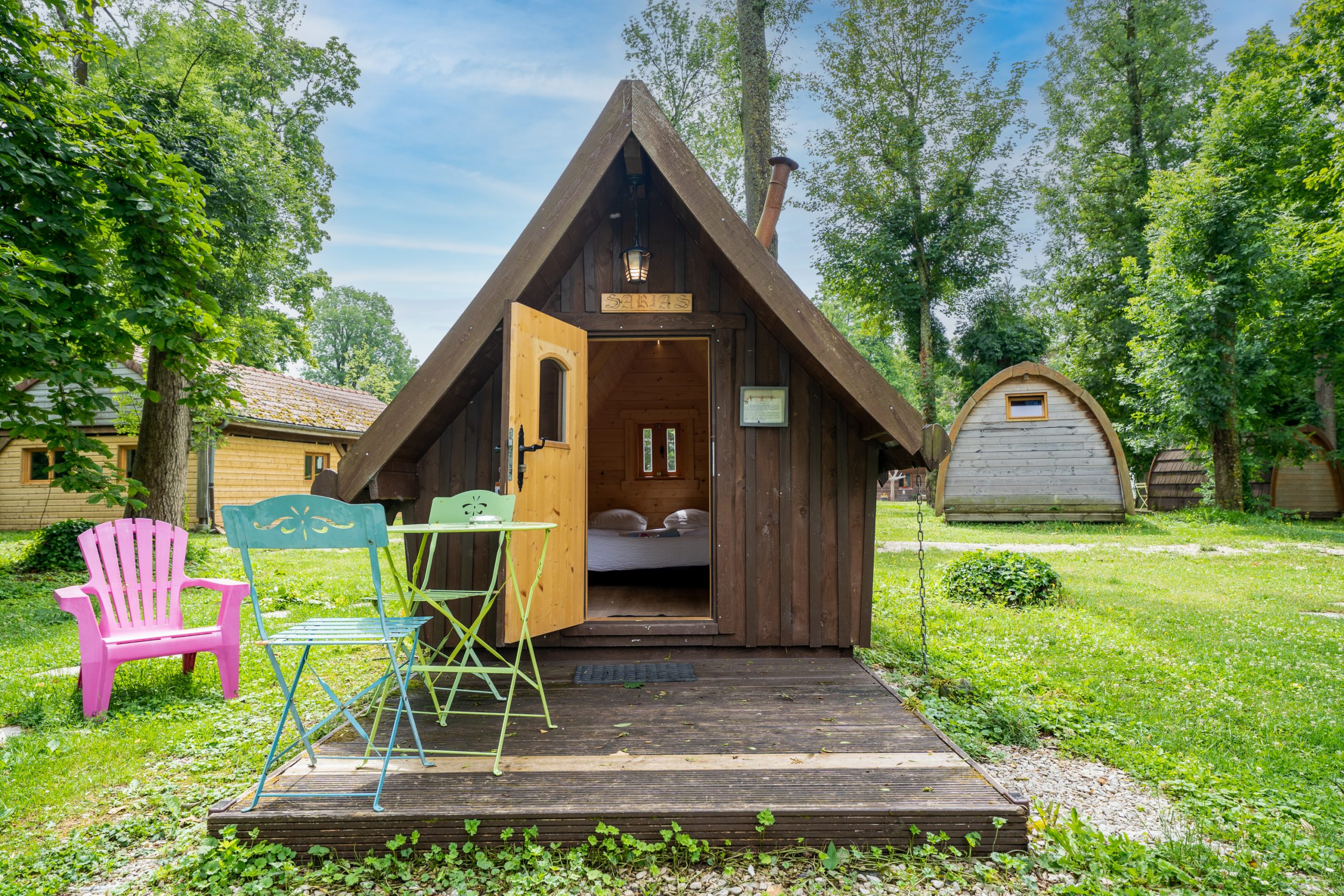 J5_6Champagne-13 Cabane en bois à Champagne-Ardenne, avec chaises colorées et verdure environnante.