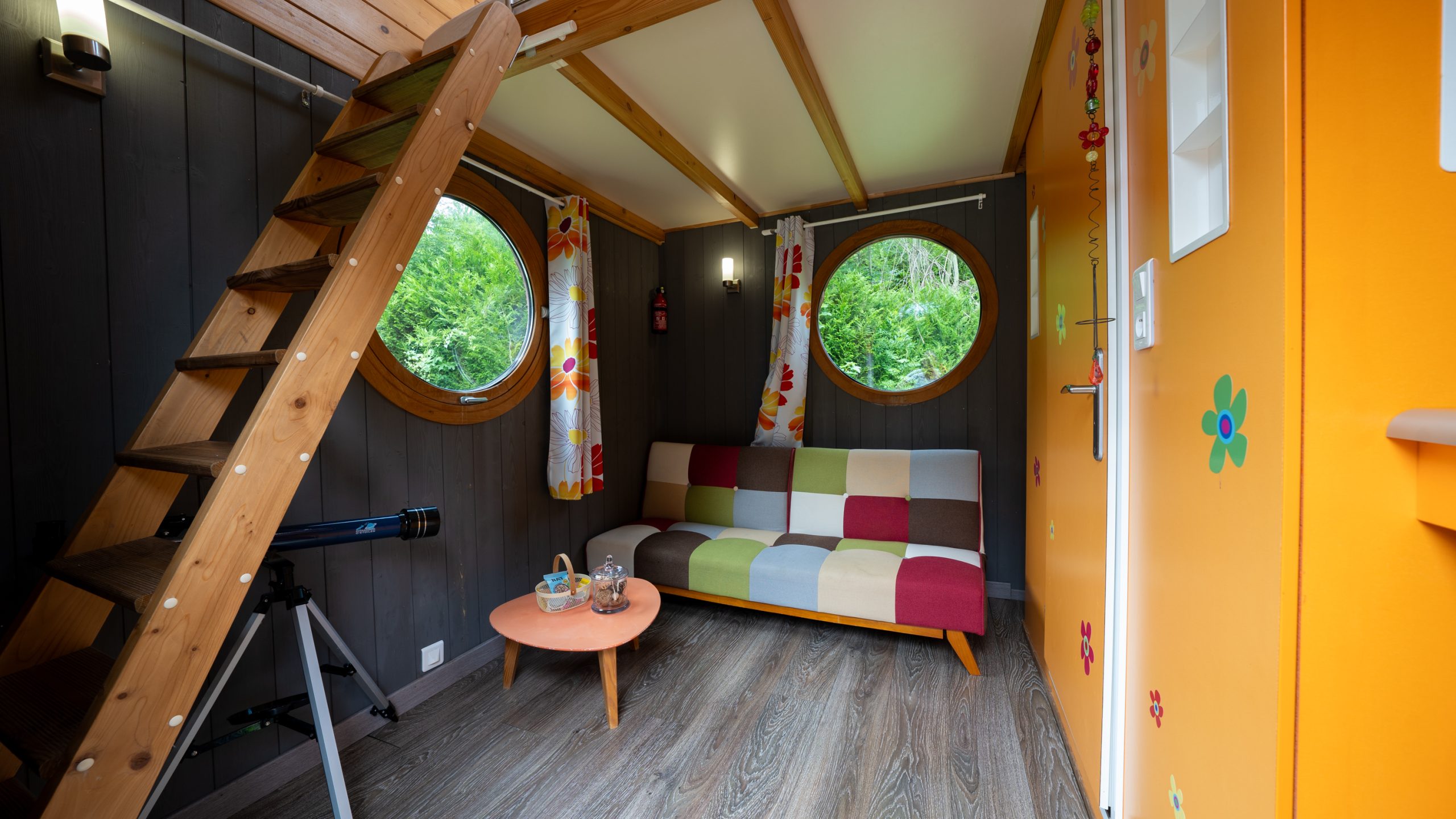 J5_6Champagne-46 Hébergement insolite à Champagne-Ardennes : cabane colorée avec fenêtres rondes et escalier en bois.