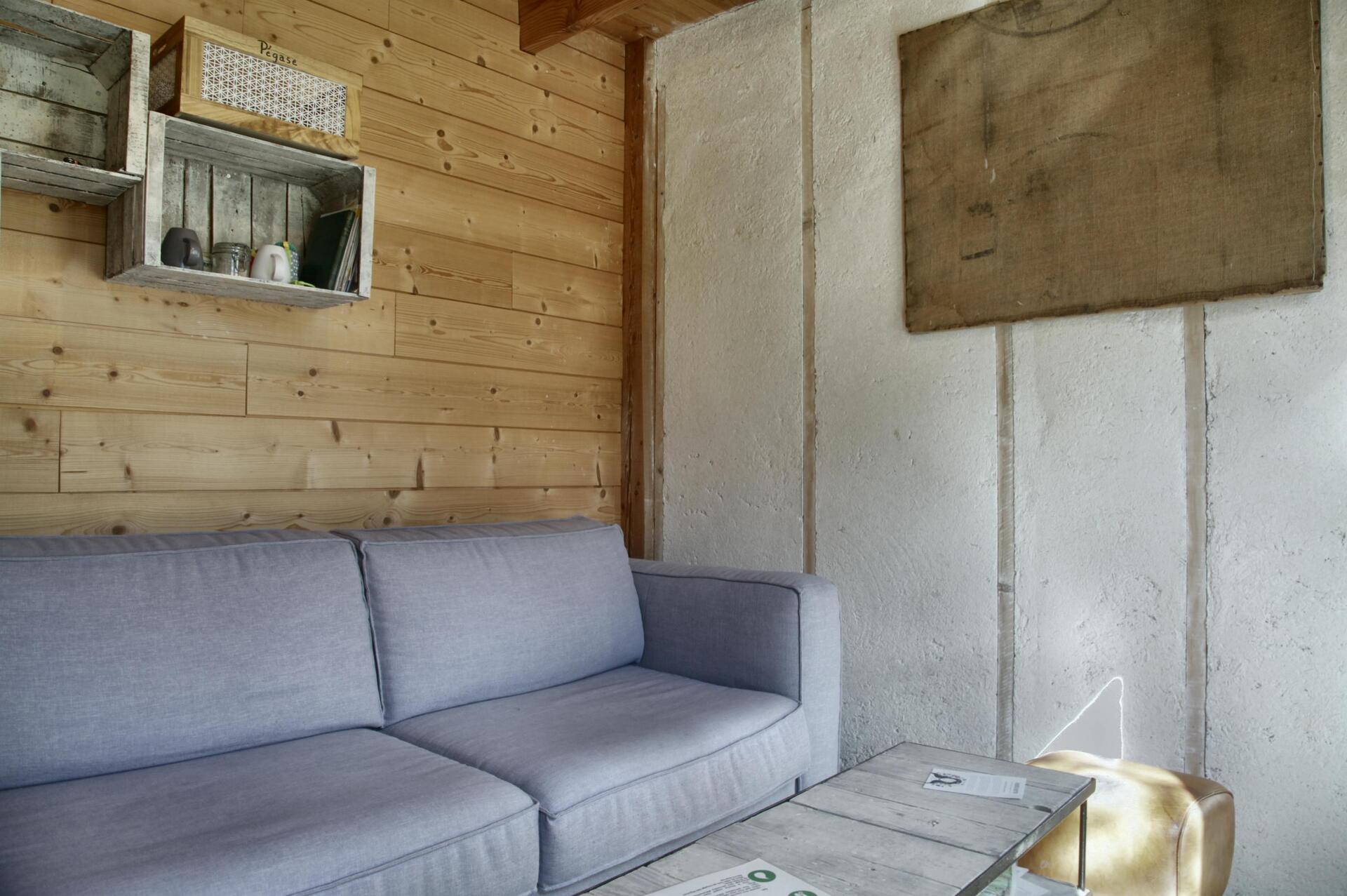 ©TerredesBaronnies-Cabane Pégase-Salon-Provence Cottage en bois avec un canapé confortable et des étagères rustiques.