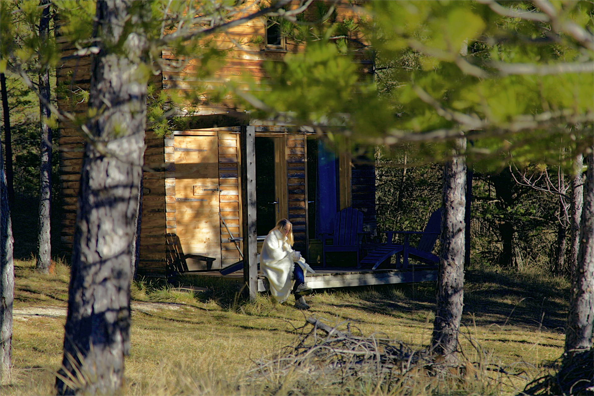 ©TerredesBaronnies-Cabane Pégase-Terrasse-Drôme Cabane en bois dans la nature, avec une personne assise sur la terrasse.