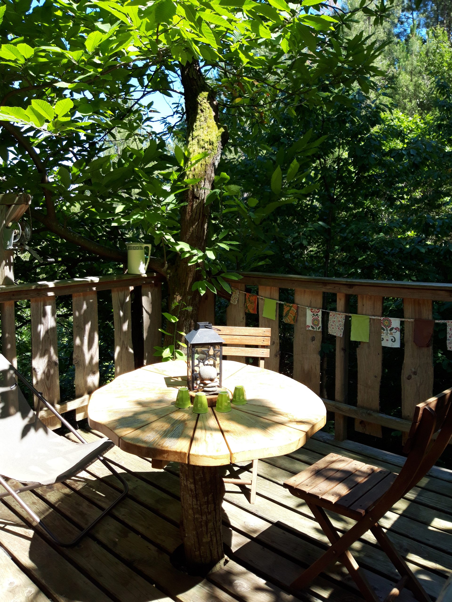 20200703_154344 Cabane perchée en bois dans les arbres, avec une table ronde et des chaises.