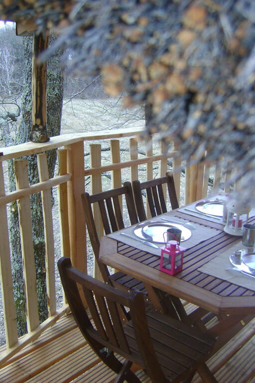 cabanes-chanteclair-la-familiale-1 (1) Cabane perchée avec terrasse en bois et table élégamment dressée.