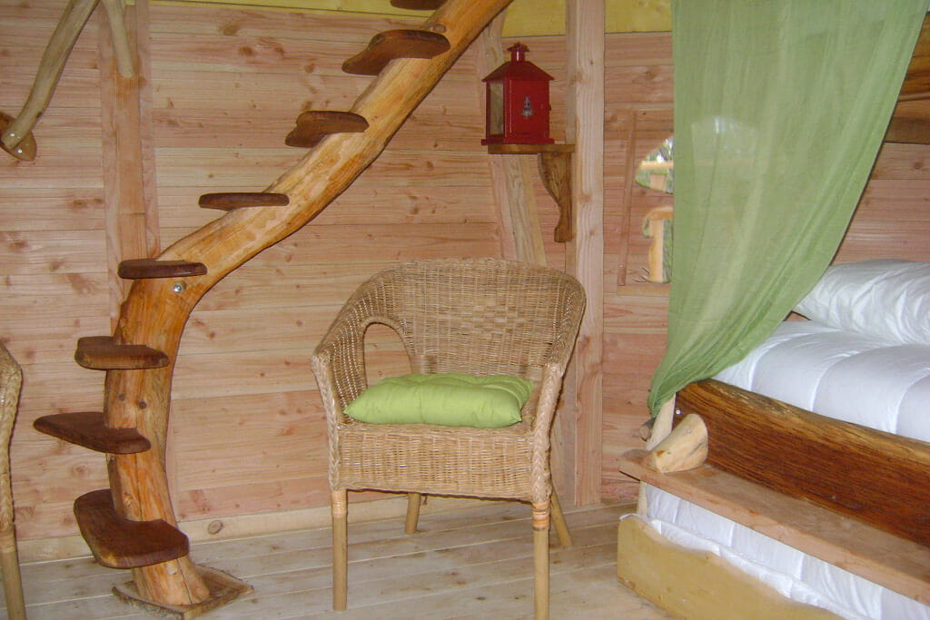 cabanes-chanteclair-la-familiale-3 Hébergement insolite en bois avec une échelle en spirale et une chaise en osier.